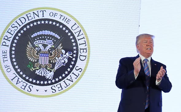 Трамп икки бошли ва гольф таёқчаларини ушлаган бургут тасвиридаги герб билан нутқ сўзлади